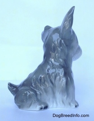 The right side of grey and white miniature Schnauzer sitting figurine. The figurine has a short tail that is arched into the air.