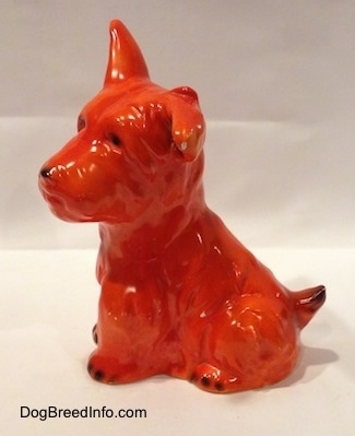 The left side of an orange Schnauzer figurine sitting. The figurine has one ear up and one ear flopped to the side.