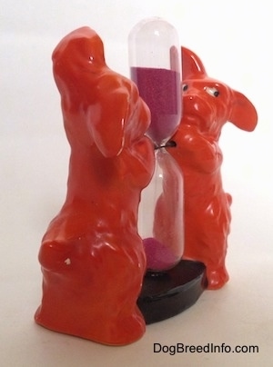 The back of one orange and the front of another orange Schnauzer figurine. Both figurines have one ear flopped over and another ear thats in the air.