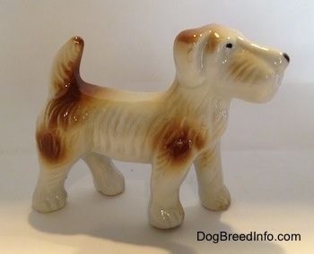 The right side of a white with brown bone china Schnauzer figurine. The figurine has black circles for eyes and a nose.