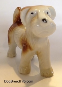 A white with brown figurine of a bone china Schnauzer. The figurine has short legs.