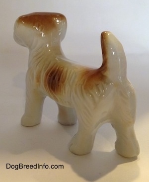 The back left side of a figurine of a white with brown bone china Schnauzer. The figurines tail is in the air.