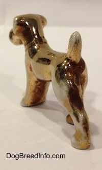 The back left side of a bone china figurine of a Schnauzer that is painted in gold. The tail of the figurine should be arched in the air.