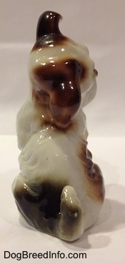 The back of a parti-colored figurine of a bone china Miniature Schnauzer in a begging pose. The figurines tail is medium length and arched above the back.