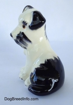 The left side of a ceramic figurine of a parti-color Miniature Schnauzer sitting. The figurine has black ears.