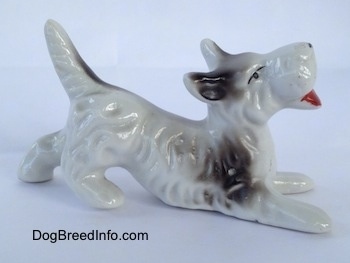 The right side of a parti-colored Schnauzer figurine in a play bow position. The figurines mouth is painted open.