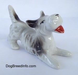The front right side of a Schnauzer figurine in a play bow pose. The figurine has black circles for eyes.