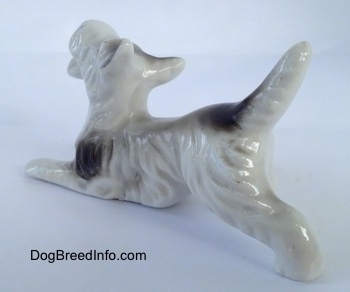 The back left side of a bone china white with black bone china Schnauzer figurines. The figurines long tail is in the air.
