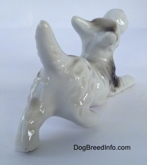 The back right side of a bone china parti-colored Schnauzer figurine in a begging pose. The figurine has long limbs.