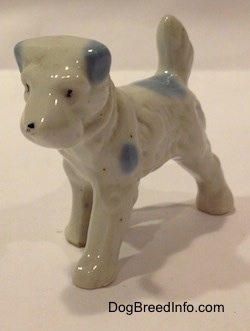 The front left side of a white with blue bone china Miniature Schnauzer figurine. This figurine has black circles for eyes.