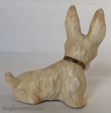 The right side of a figurine of a white and cream Scottish Terrier figurine. The Scottish Terrier has a brown collar on.
