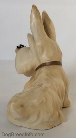 The back left side of a figurine of a white and cream Scottish Terrier sitting. The figurine has a short curly tail.
