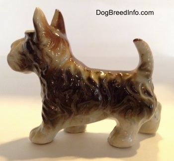 The left side of a figurine of a brown with white bone china Scottish Terrier. The figurine has fine hair details along its head and body.