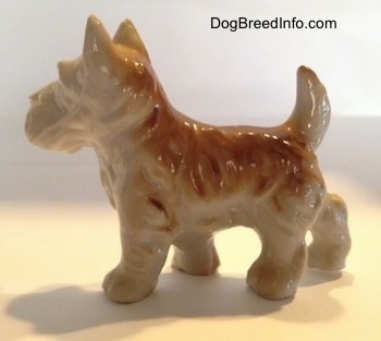The left side of a brown and white figurine of a bone china Scottish Terrier. The figurines tail is arched into the air.