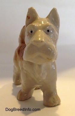 A brown and white bone china Scottish Terrier figurine. The figurine has small black circles for eyes.