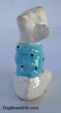 The back of a white ceramic Scottish Terrier that is sitting with a blue with black shirt on figurine. The figurine has a short tail on its back.