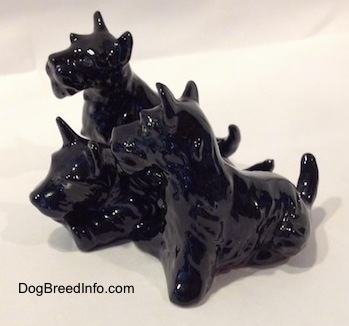 The front left side of a black Scottish Terrier figurine trio. The figurines tails are arched into the air.