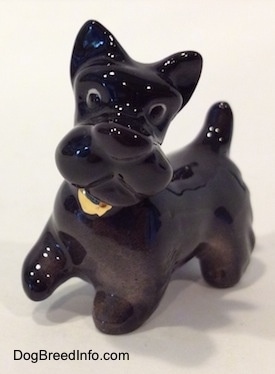 The front left side of a black figurine of a Scottish Terrier walking. The figurine has its front right paw in the air.