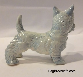 The right side of a white figurine of a Scottish Terrier with blue highlights. The figurine has its tail in the air.