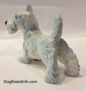 The back left side of a figurine of a white with blue Scottish Terrier. The figurines body is longer than its legs.