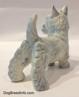 The back right side of a white with blue highlights Scottish Terrier figurine. The figurine has a the blue stamp of Goebel W.Germany on the back of its leg.