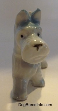 A white bone china Scottish Terrier figurine with blue ears. The figurine has small black circles for eyes.