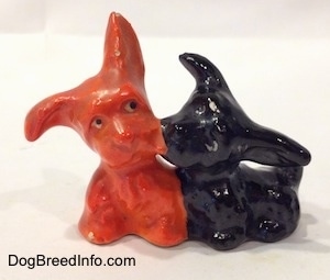 A black Scottish Terrier figurine and an orange Scottish Terrier figurine that are playing. The ears of the figurines are white circles with black circles inside of them.