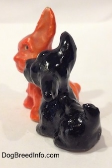The left side of an orange figurine and a black figurine of Scottish Terriers that are playing together. The figurines tails are arched over there backs.