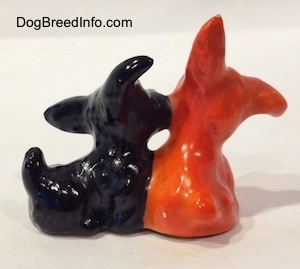 The back of a black Scottish Terrier figurine and an orange Scottish Terrier figurine. The orange figurine is in a sitting position.