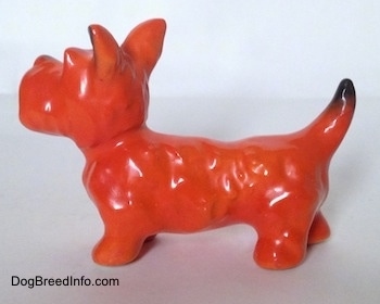 The left side of an orange with black figurine of a Scottish Terrier. The figurine has fine hair details along its body.