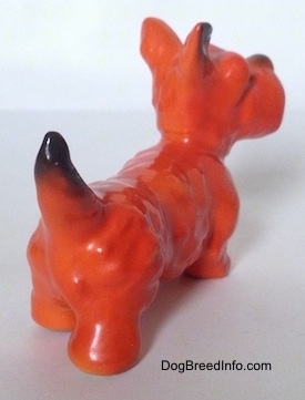 The back right side of an orange and black Scottish Terrier figurine. The figurine has short legs.