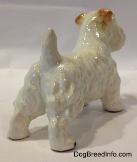 The back right side of a white Sealyham Terrier figurine. The ears of the figurine are brown and flopped over.