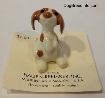 A figurine of a white and brown Mini Curbstone Setter puppy that is in a begging pose.