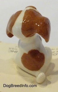 The back of a figurine of a white and brown Mini Curbstone Setter puppy that is in a begging pose. The figurine has a short arched up white tail.