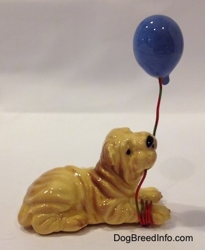 The right side of a Shar-Pei lying figurine with a blue balloon in its mouth.