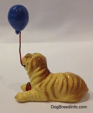 The left side of a brown and tan figurine of a Shar-Pei lying position with a blue balloon in its mouth. The figurine has fine wrinkle details.