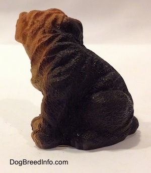 The left side of a black with brown figurine of a Shar-Pei puppy in a sitting position. The figurine has wrinkle details along its body.