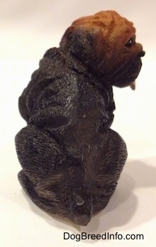 The back of a figurine of a black with brown Shar-Pei puppy figurine in a sitting position. The figurine has a small tail.