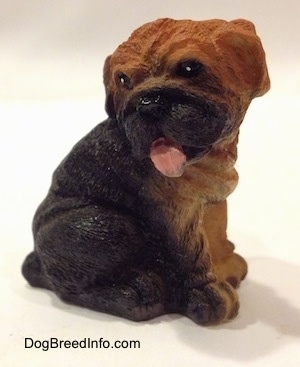 The front right side of a black with brown figurine of a Shar-Pei puppy that is made out of resin. The figurine has black circles with white dots for eyes.