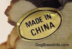 Close up - On the underside of a figurine of a Shar-Pei puppy is the a gold sticker that reads 'Made in China'.