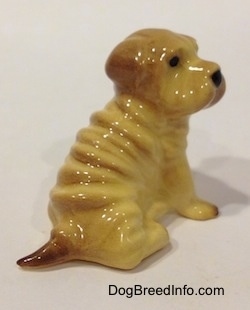 The back right side of a figurine of a Chinese Shar-Pei sitting. The figurine has a short brown tail.