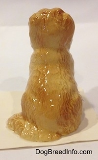 The back of a tan with brown Sheepdog that is in a sitting pose figurine. The figurine has a long fluffy tail.