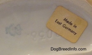 The underside of a Shepherd figurine that has number engraved on it and above the engraving is a sticker that reads 'Made in East Germany'.