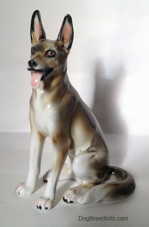 The front left side of a brown and white with black German Shepherd sitting figurine. The tongue of the figurine is sticking out.