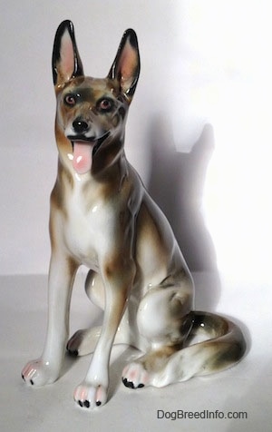 A figurine of a brown and white with black German Shepherd sitting. The figurine has its ears in the air.