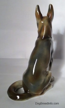 The back of a brown and white with black figurine of a German Shepherd sitting. The figurine is glossy.