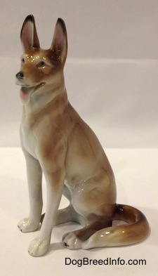 The left side of a brown and white German Shepherd sitting figurine. The figurine has its long tail wrapped around its left side.