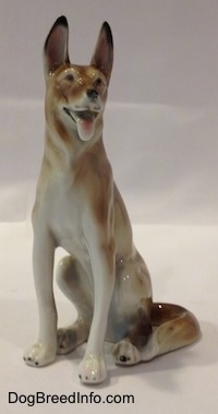 The front left side of a sitting brown with white German Shepherd figurine. The figurine has its tongue out and black circles for eyes.
