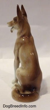 The back left side of a figurine of a brown and white sitting German Shepherd. The figurine has perky ears.