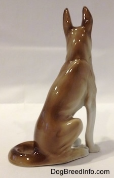 The back right side of a brown and white German Shepherd sitting figurine. The figurine is glossy.